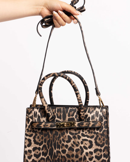 Leopard print handbag with a detachable shoulder strap and gold accents, held by hand.