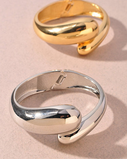 Polished gold metal bangle featuring a modern twist design

